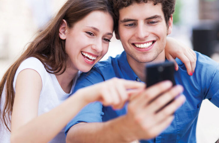 Pareja mirando un teléfono celular y sonriendo