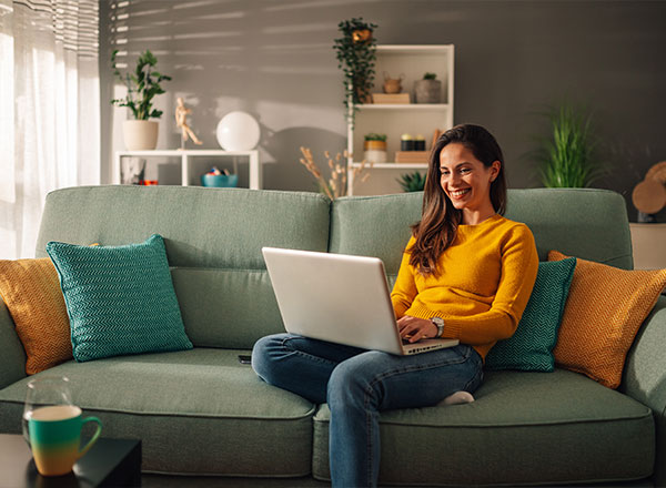 mujer sentada en su sofá usando su computadora y sonriendo